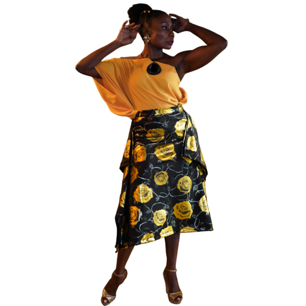 Model is wearing a one shoulder tulle material yellow blouse, and a flowery patterned skirt.